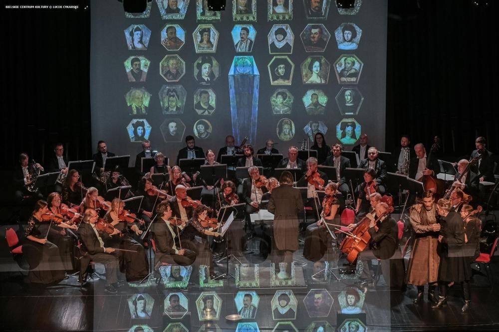 Polska Opera Królewska wykonuje "Straszny dwór" Moniuszki, artyści ubrani są w kolorowe stroje z epoki, orkiestra akompaniuje ubrana w czarne stroje