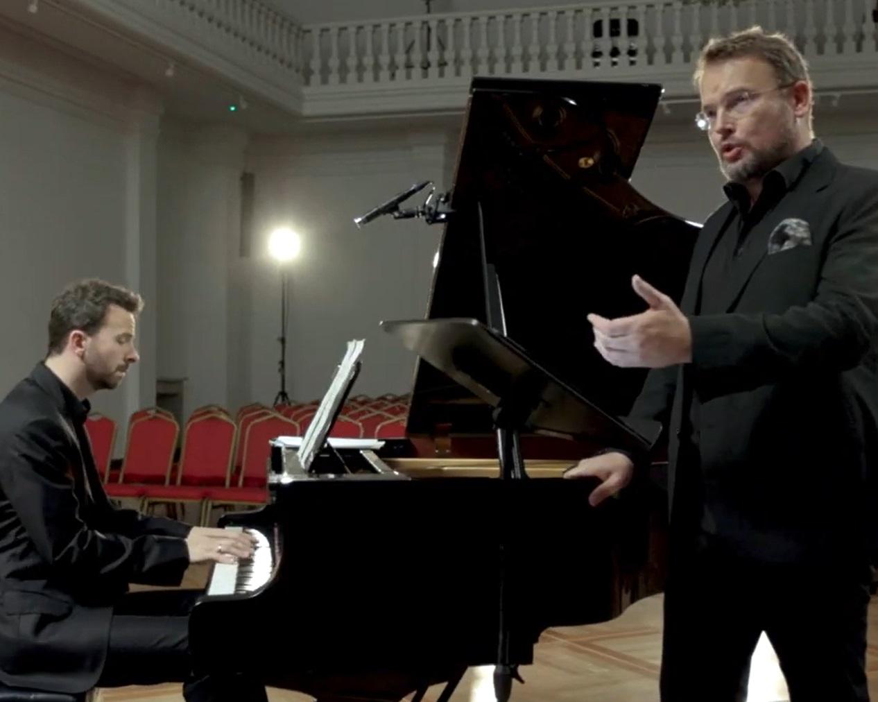 Bas baryton Tomasz Konieczny wykonuje pieśni Moniuszki z pianistą Lechem Napierałą, są ubrani w czarne stroje i muzykują przy czarnym dużym fortepianie