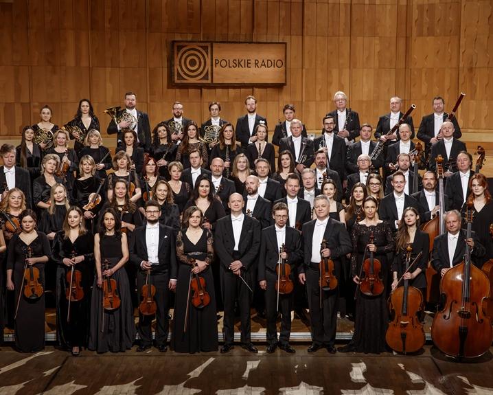 Orkiestra Polskiego Radia, muzycy ubrani w czarne sukienk i fraki stoją w czterech rzędach na estradzie