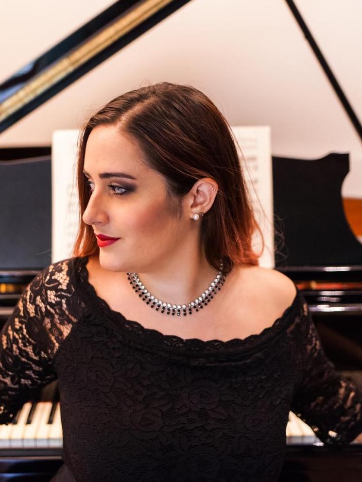 Włoska pianistka Armellini pozyje na tle fortepianu, jest ubrana w czarną sukienkę i nosi czarno-srebrny naszyjnik